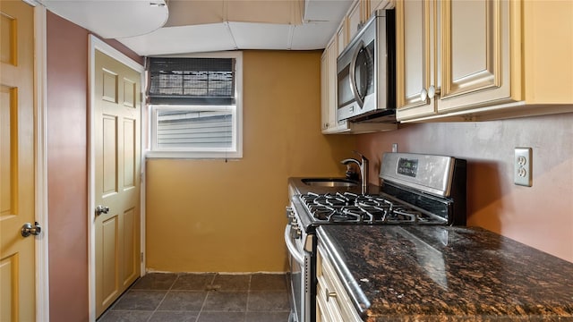 kitchen featuring dark stone counters, cream cabinets, dark tile patterned flooring, sink, and stainless steel appliances