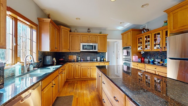 kitchen with sink, backsplash, dark stone countertops, appliances with stainless steel finishes, and light wood-type flooring