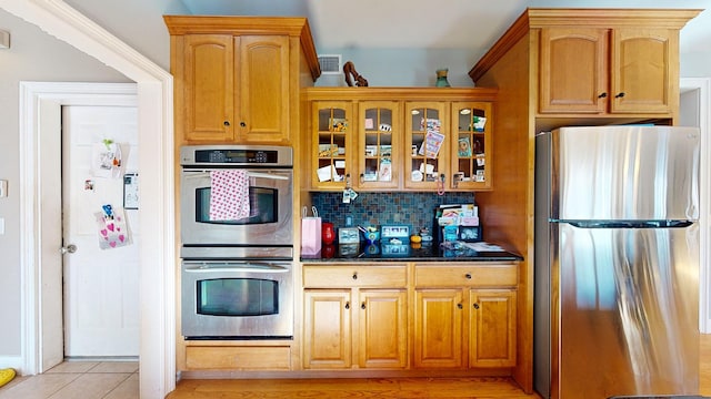 kitchen featuring backsplash, dark stone countertops, light tile patterned floors, and appliances with stainless steel finishes