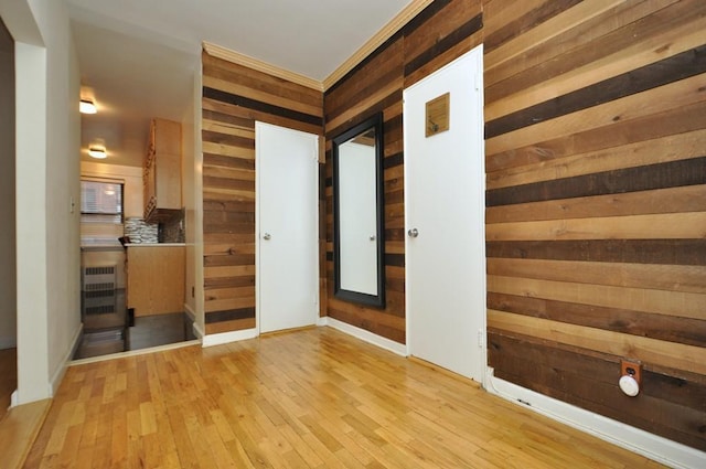 hallway with light wood-type flooring, crown molding, and wooden walls