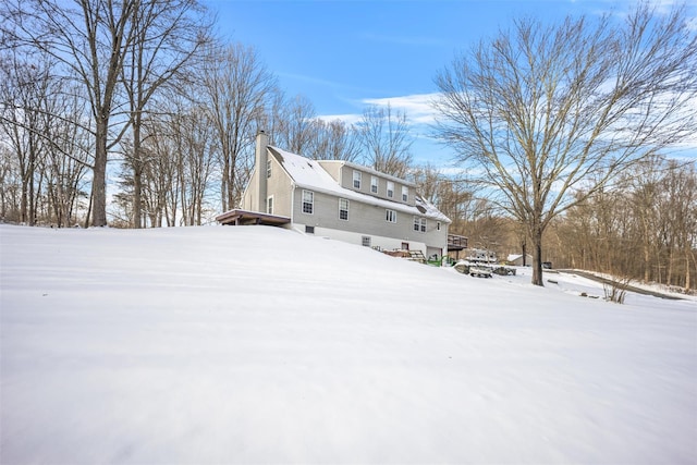 snow covered property with a wooden deck and a chimney