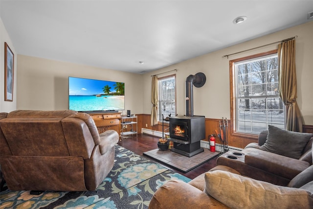 living room featuring a wood stove, visible vents, wood finished floors, a baseboard heating unit, and wainscoting