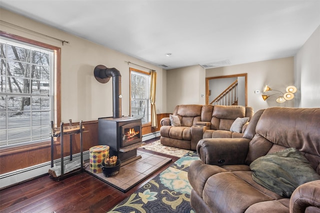living area with dark wood-type flooring, visible vents, a wood stove, and a baseboard heating unit