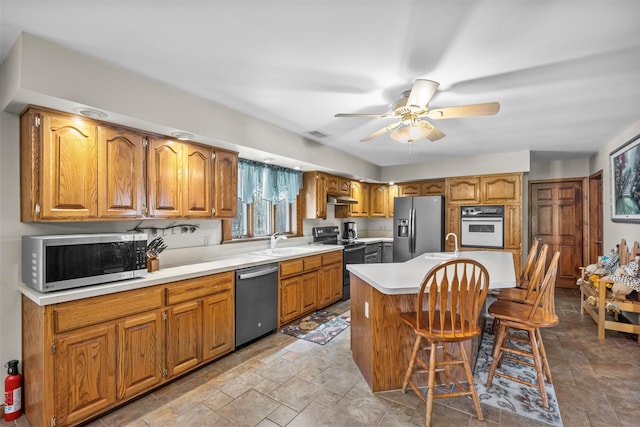 kitchen featuring stone finish floor, under cabinet range hood, light countertops, a sink, and stainless steel appliances