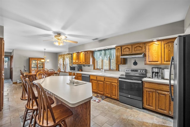 kitchen with a sink, appliances with stainless steel finishes, stone finish floor, and under cabinet range hood