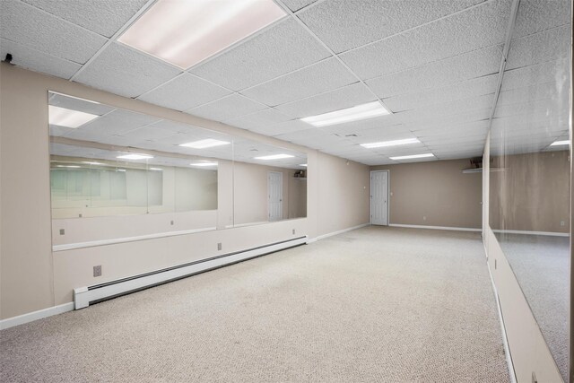 basement featuring baseboard heating, a paneled ceiling, baseboards, and carpet