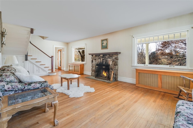 living room with a stone fireplace, radiator, a wealth of natural light, and light hardwood / wood-style flooring