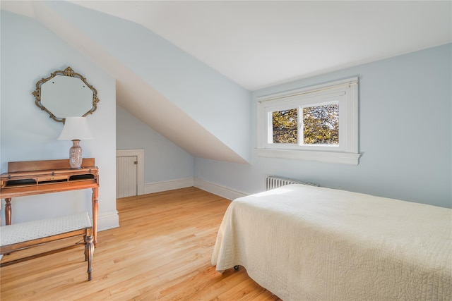 bedroom featuring radiator, light hardwood / wood-style floors, and vaulted ceiling