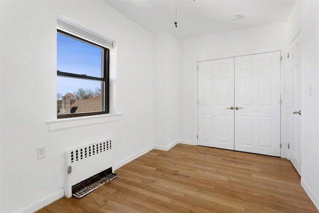 unfurnished bedroom featuring radiator heating unit, light hardwood / wood-style flooring, and a closet