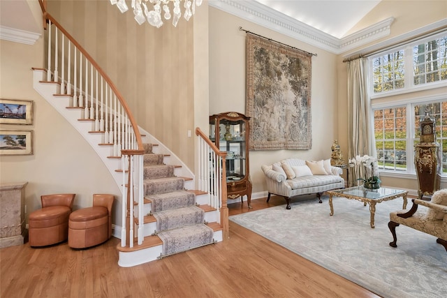 living area featuring wood-type flooring, an inviting chandelier, high vaulted ceiling, and ornamental molding