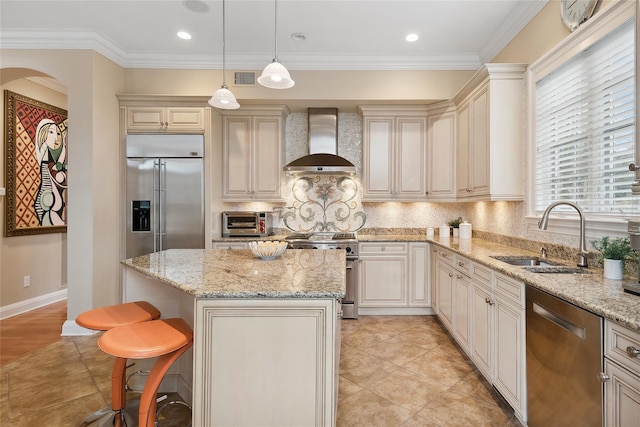 kitchen featuring light stone countertops, stainless steel appliances, sink, wall chimney range hood, and hanging light fixtures