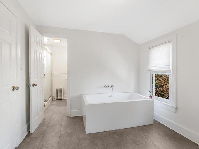 bathroom with tile patterned floors, a tub, radiator heating unit, and vaulted ceiling