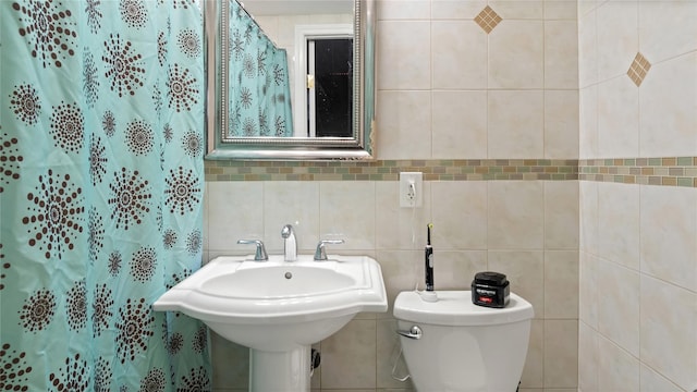 bathroom with curtained shower, sink, tile walls, and toilet