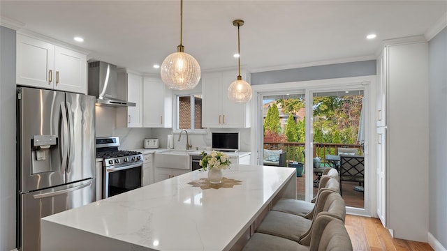 kitchen featuring wall chimney exhaust hood, stainless steel appliances, light hardwood / wood-style flooring, white cabinets, and hanging light fixtures