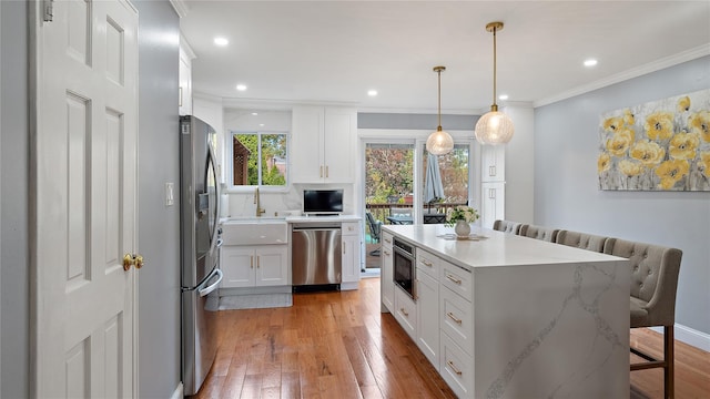 kitchen with white cabinetry, hanging light fixtures, light hardwood / wood-style flooring, a kitchen bar, and appliances with stainless steel finishes