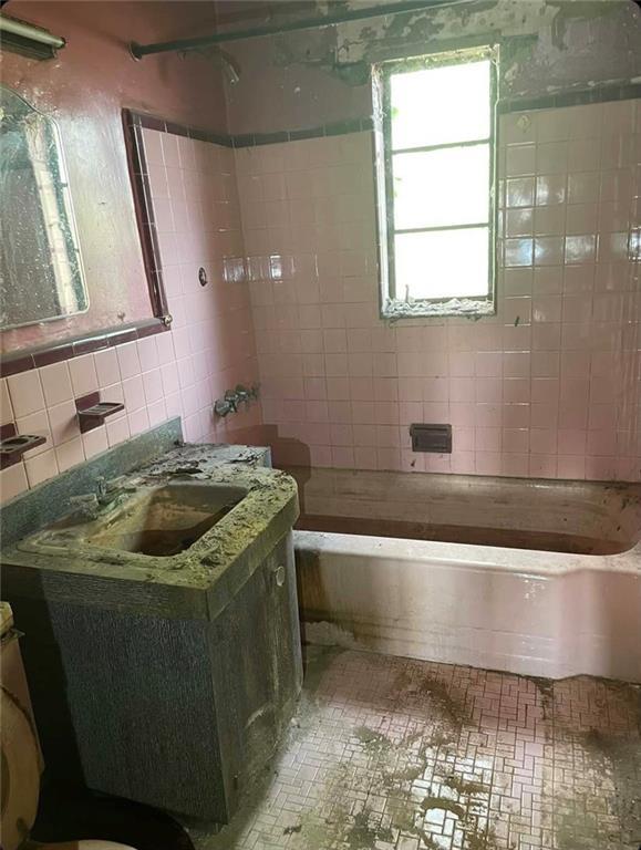 full bathroom featuring tiled shower / bath, vanity, tile walls, and toilet