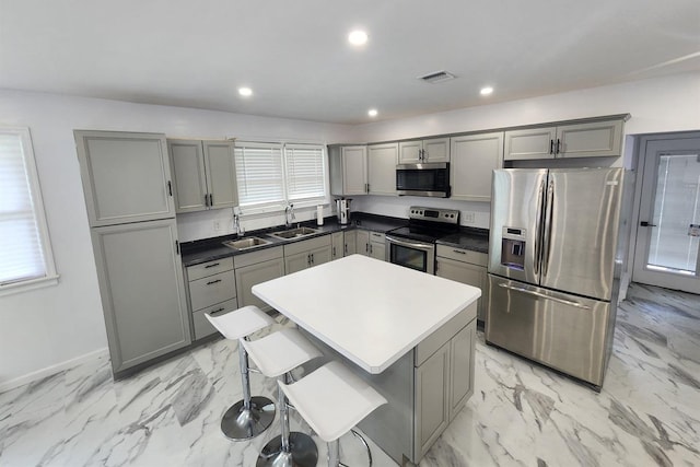 kitchen featuring a kitchen bar, appliances with stainless steel finishes, gray cabinets, and a kitchen island