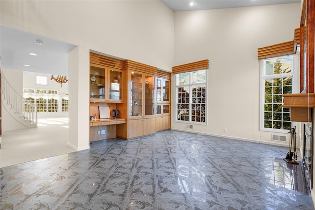 unfurnished living room with carpet flooring, a healthy amount of sunlight, a towering ceiling, and an inviting chandelier