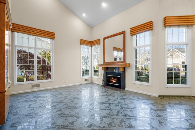 unfurnished living room featuring high vaulted ceiling, a healthy amount of sunlight, and a premium fireplace