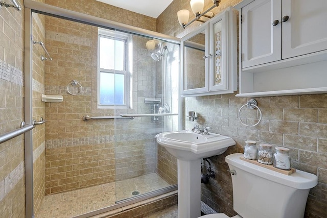 bathroom with sink, tasteful backsplash, toilet, a shower with shower door, and tile walls