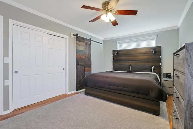 bedroom with crown molding, light hardwood / wood-style flooring, ceiling fan, a barn door, and a closet