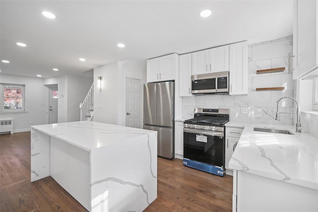 kitchen with light stone countertops, appliances with stainless steel finishes, sink, white cabinets, and a center island