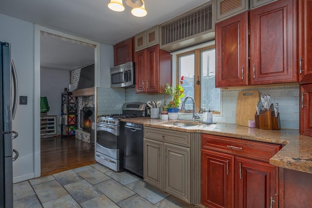 kitchen with a fireplace, stainless steel appliances, sink, light stone counters, and decorative backsplash