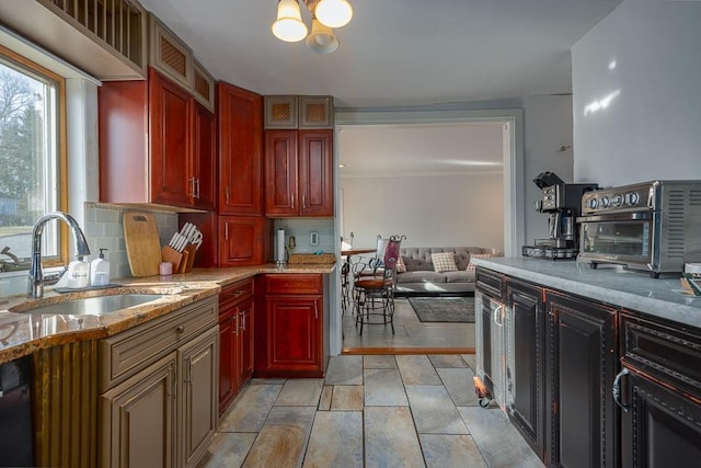 kitchen with black dishwasher, light stone countertops, an inviting chandelier, sink, and backsplash