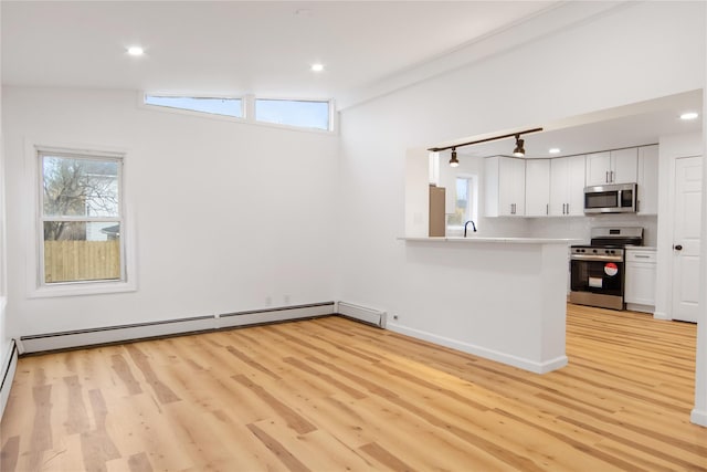 kitchen with stainless steel appliances, baseboard heating, light hardwood / wood-style flooring, white cabinets, and lofted ceiling