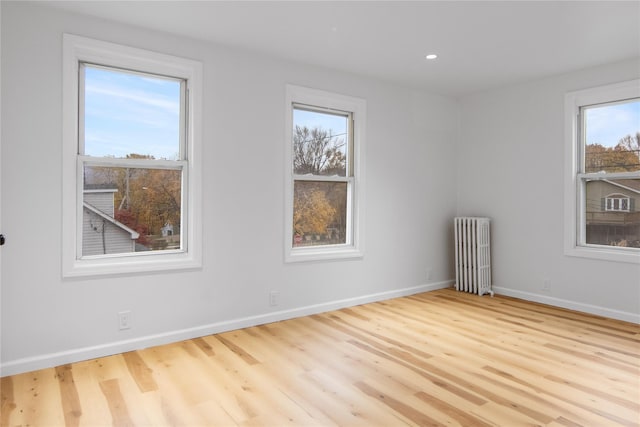 unfurnished room featuring radiator heating unit, a wealth of natural light, and light hardwood / wood-style flooring