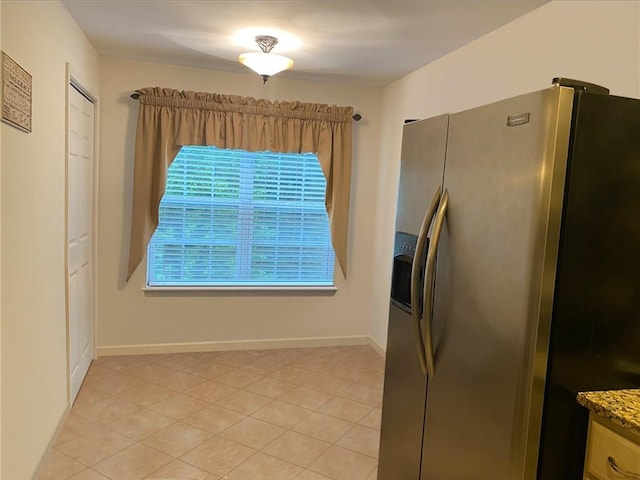 kitchen with stainless steel fridge, light tile patterned flooring, and stone counters