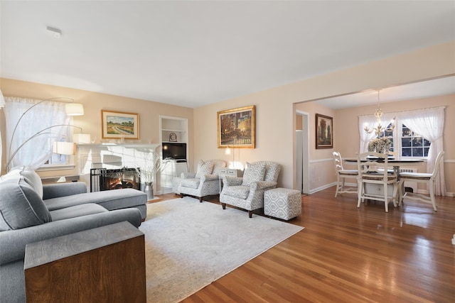 living area featuring baseboards, a lit fireplace, wood finished floors, and a notable chandelier