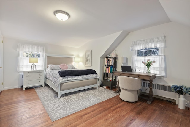 bedroom with lofted ceiling, radiator heating unit, and wood finished floors