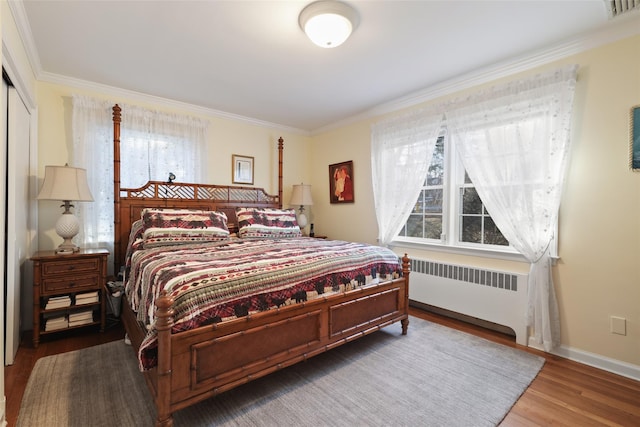 bedroom with wood finished floors, visible vents, baseboards, radiator, and crown molding