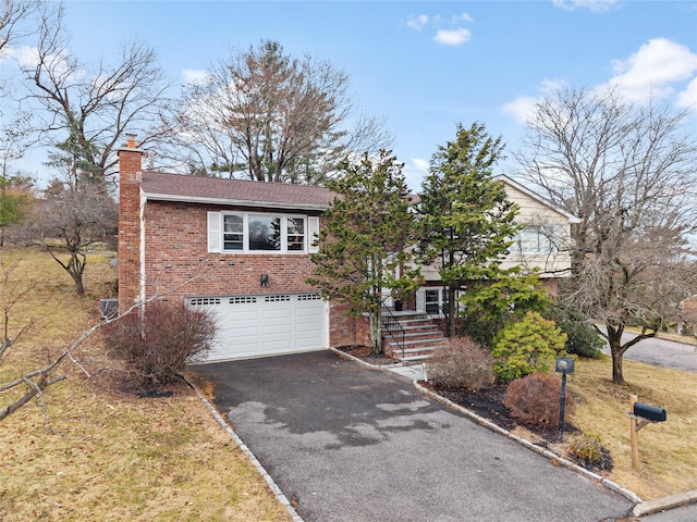 view of front of property featuring brick siding, aphalt driveway, a garage, and a chimney