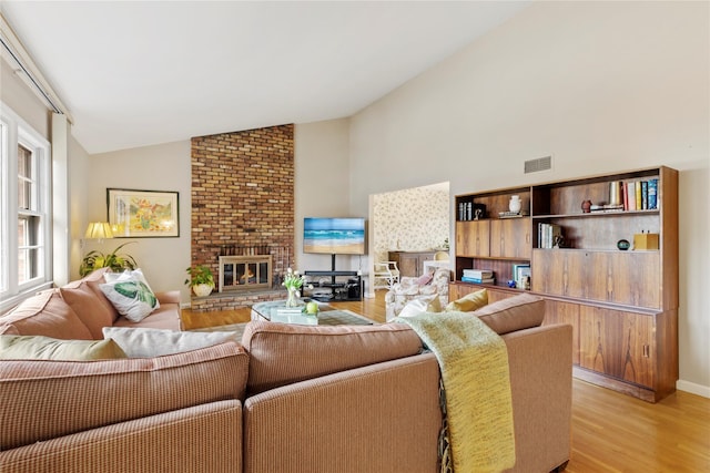 living room featuring a brick fireplace, visible vents, light wood finished floors, and high vaulted ceiling