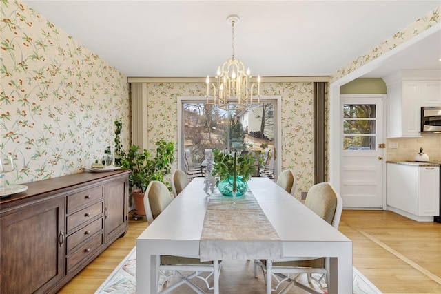 dining area with light wood finished floors, wallpapered walls, and an inviting chandelier