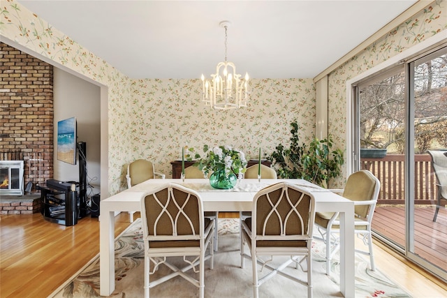 dining room with wallpapered walls, a brick fireplace, wood finished floors, and a chandelier