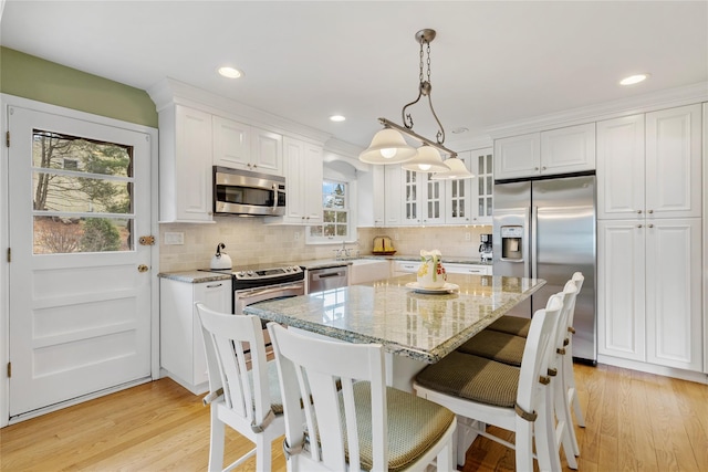 kitchen featuring appliances with stainless steel finishes, white cabinetry, glass insert cabinets, and light stone countertops