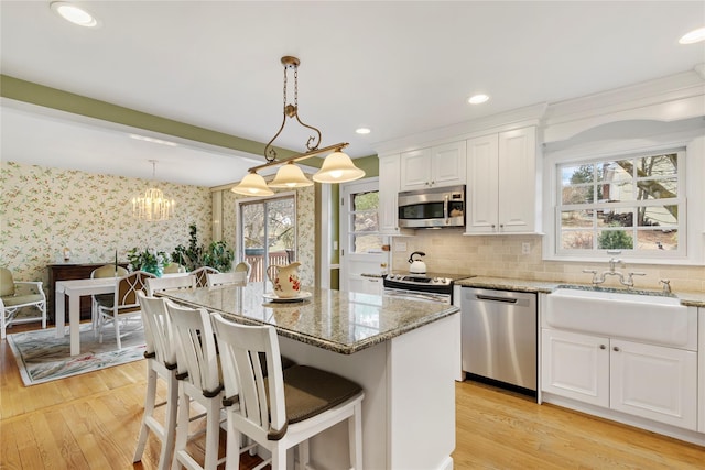 kitchen with a sink, appliances with stainless steel finishes, white cabinets, wallpapered walls, and light stone countertops