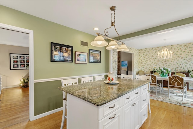 kitchen featuring visible vents, wallpapered walls, a kitchen breakfast bar, light wood-style floors, and white cabinets