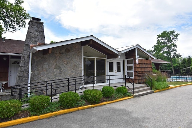 view of front of house with fence, stone siding, and a chimney