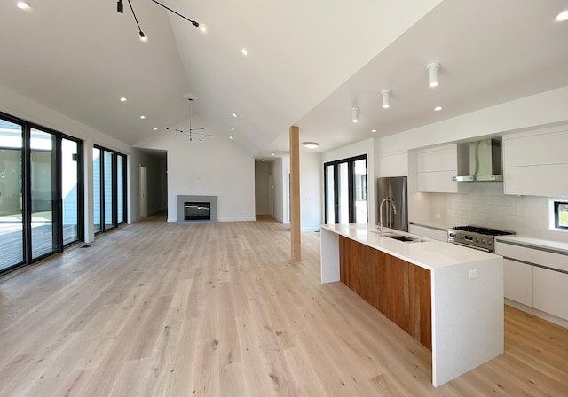 kitchen featuring white cabinetry, sink, a large island, wall chimney range hood, and light wood-type flooring