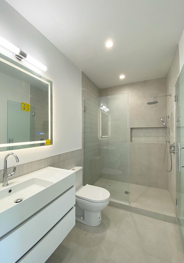 bathroom with vanity, toilet, walk in shower, and tile walls