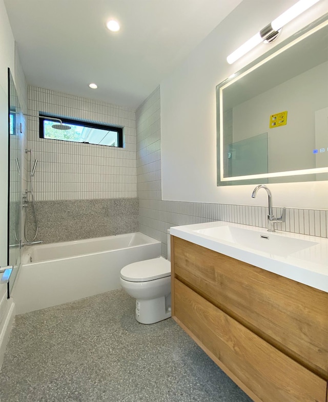 full bathroom with vanity, toilet, tiled shower / bath, and tile walls