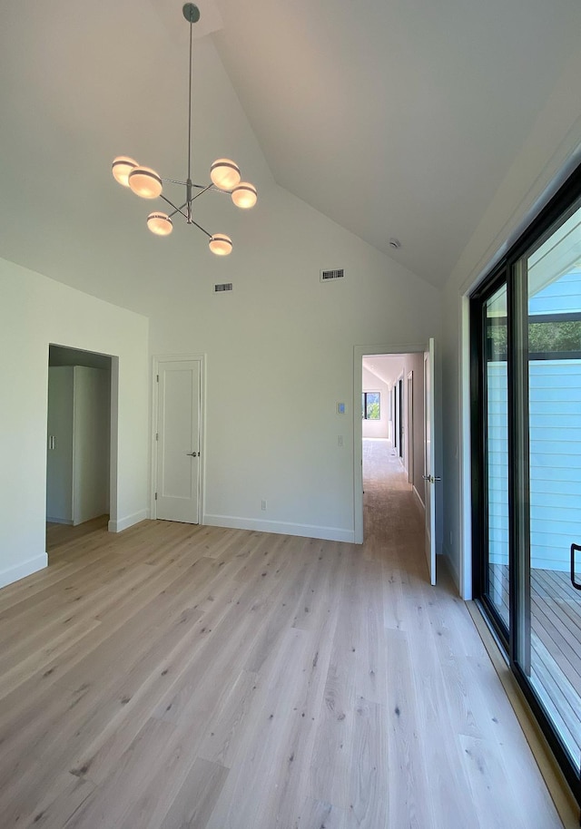 empty room with light wood-type flooring, high vaulted ceiling, and a chandelier