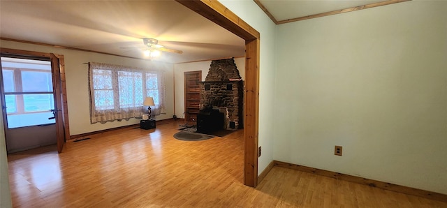 unfurnished living room with ceiling fan, a wood stove, crown molding, and light hardwood / wood-style flooring