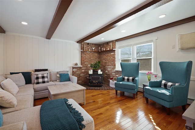 living room featuring hardwood / wood-style flooring, a baseboard heating unit, beam ceiling, and a wood stove