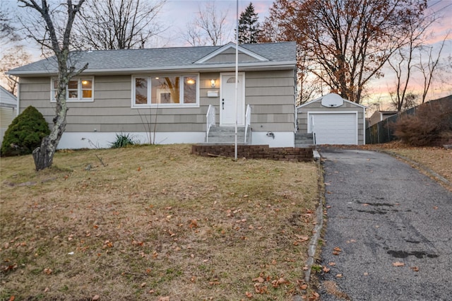 view of front of home featuring aphalt driveway, an outdoor structure, a detached garage, and a lawn