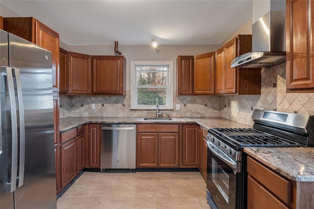 kitchen featuring stainless steel appliances, a sink, wall chimney range hood, light stone countertops, and brown cabinetry